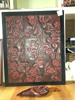 Photo of a framed large wood carved floral art panel consisting of 12 individual segments with reddish-brown hand-carved flowers and leaves.