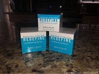 Photo showing two unopened Redefine Lip Renewing Serum boxes and one unopened Redefine Multi-Function Eye Cream box on a granite countertop.