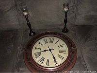 Wall clock with bronze finish, Roman numerals, and decorative text 'Live, Laugh, Love' on the rim; placed alongside two matching bronze look candle holders with glass candle cups