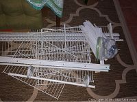 Photo showing disassembled white wire shelving panels, support brackets, rods, and hardware arranged on the floor.