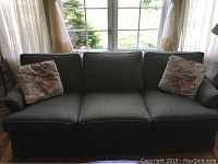 Front view of three-seat sofa in front of window, showing full length and two throw pillows