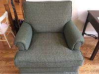 Front view of the green upholstered arm chair on a hardwood floor, showing rolled arms and cushioned backrest.