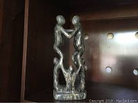 Front view of soapstone sculpture showing four connected human figures on a wooden shelf with perforated back panel.
