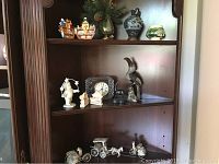 Wide shot of wooden shelf showing assorted collectibles including porcelain figurines, ceramic vases, a clock, and silver filigree animal and human figures