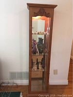Front view of oak curio cabinet showcasing glass front door and interior shelves with mirrored back and displayed items inside (not included).