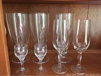 Six clear stem glasses of different sizes displayed against wood background.