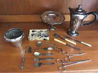 Photo showing wide assortment of silver plated serving ware including ice bucket, serving platter, coffee pot, cutlery and specialized utensils