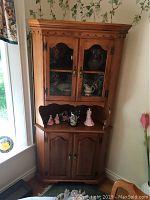 Full view of maple corner cabinet showing upper glass doors and lower wooden doors with decorative scalloped trim.