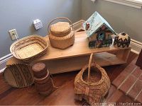 Wide view showing assorted woven baskets arranged on and around a low wooden stand with wheels against a corner wall.