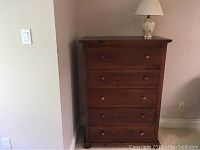 Pine 5-drawer dresser with wooden knobs, shown with accent lamp on top.