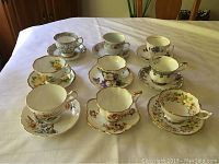 Photo showing all 9 china tea cups and matching saucers arranged on table, each with distinct floral pattern and gold accents