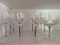 Clear crystal wine glasses with slender stems arranged in a row on a white shelf.