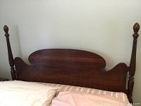 Full front view of the cherrywood queen size headboard with central curved panel and two tall turned posts with finials.