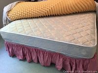 Top view of queen mattress with a yellow egg crate foam topper, red and white striped mattress skirt