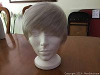 Front view of a platinum short wig on a white mannequin head, showing the hair texture and ear length style.