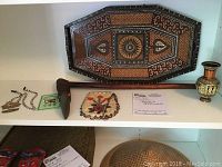 Overview of travel souvenirs including wooden tray, decorative axe, brass vase, fabric pouch, and basket on shelf