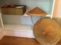 Shelf showing two straw hats and a decorative box with small ornamental red shoes on top.