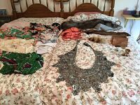 Overview of multiple vintage clothing pieces, fur stoles, sunglasses, and other accessories arranged on a bed.