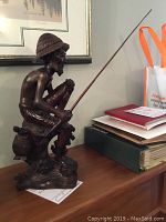 Side view showing the detailed carving and posture of the fisherman seated with fishing rod.