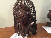 Front view showing detailed face and headdress of carved Indonesian goddess sculpture on wooden surface.