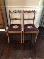 Pair of vintage wooden side chairs with tapestry seats showing floral embroidery and curved backrest design.