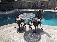 Overview of metal bistro table and two chairs on stone patio by pool