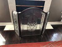 Front view of three-panel folding fireplace screen with decorative clear textured and beveled glass in metal frame positioned in front of fireplace.