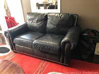 Full front view of black leather loveseat showing nail head trim on base and rolled arms