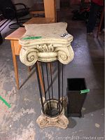 Plaster cast plant stand with classical design and metal umbrella stand placed on the floor with concrete surface.