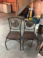 Two outdoor occasional chairs with metal frames and plastic wicker seats shown side by side, with circular stone mosaic detail on backrests.