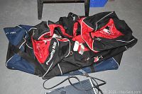 Two hockey bags lying on the floor, one red and black with logos, one navy blue.