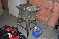 Craftsman table saw with metal stand, showing wear and use, alongside blue bin of assorted hand tools