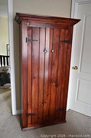 Full front view of wooden cabinet showing double doors with vertical wood plank design and metal hinges and knobs.