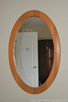 Oval wooden framed mirror hung on a wall, showing overall shape and wood tone