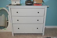 White dresser with three drawers, flat top surface with items on top, seen from front and side angles