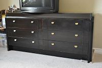Front view of black wooden dresser with 8 drawers and cream semi-circular pulls, showing general wear and scratches.