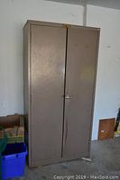 Full view of the tall beige metal storage cabinet showing two closed doors with some surface wear.