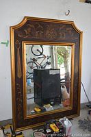 Full view of the large wood framed mirror showing the decorative gold leaf patterns and overall wood frame shape and size.