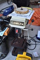 Front view of the drill press showing the Delta logo, drill table, and buffing wheel attachment on top.