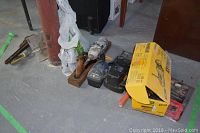 Tools laid on concrete floor including DeWalt box, charger, wooden plane, wrench, drill, and others