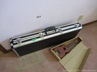 Closed black hard shell instrument case with silver trim and latch hardware next to boxed ukulele