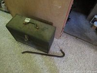 Closed green metal toolbox on carpet with crowbar alongside