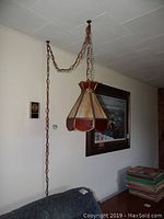 Wide view showing stained glass swag lamp suspended by a long metal chain against a white ceiling and wall.