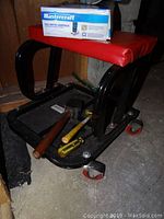 Photo showing red and black wheeled shop seat with Mastercraft multimeter box on top and hammer, screwdriver, and mallet on the lower shelf.