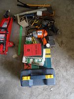 View of electric drill, hand drill, hammers, pliers, saw, books, and tool case on concrete floor.