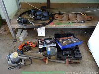 Wide view showing air compressor, electric sander, cordless spiral saw, battery packs, diamond carbide blade in packaging, pipe clamp, leather tool belt and straps on a wooden workbench.
