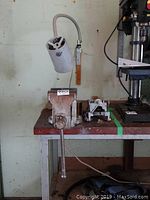 Photo of large metal vise with lever handle mounted on wooden top work bench with stainless steel frame and a mounted adjustable work light above