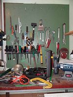 Overall view of pegboard with wrenches, screwdrivers, clamps, and power tools on bench below.