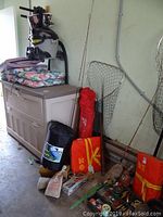 Photo showing fishing rods, nets, boat seat, storage box, and various fishing and camping gear placed on floor and against wall.