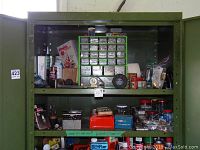 Full view of the two green metal shelves holding various hardware items, small drawers with screws and fasteners, plastic caddy with screws and bolts, several cans, and tools.